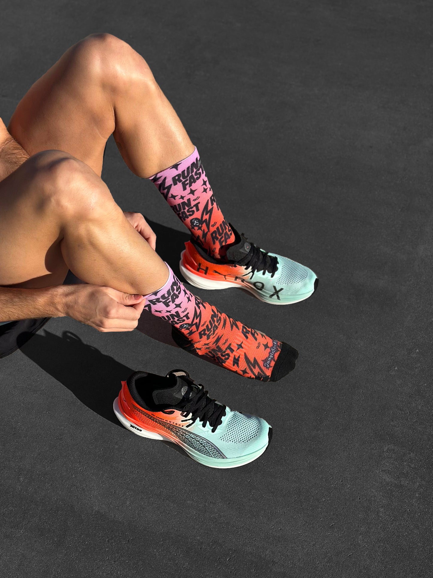 Calcetines técnicos de running sin costuras, diseño gradiente rosa a naranja con texto y rayos negros.